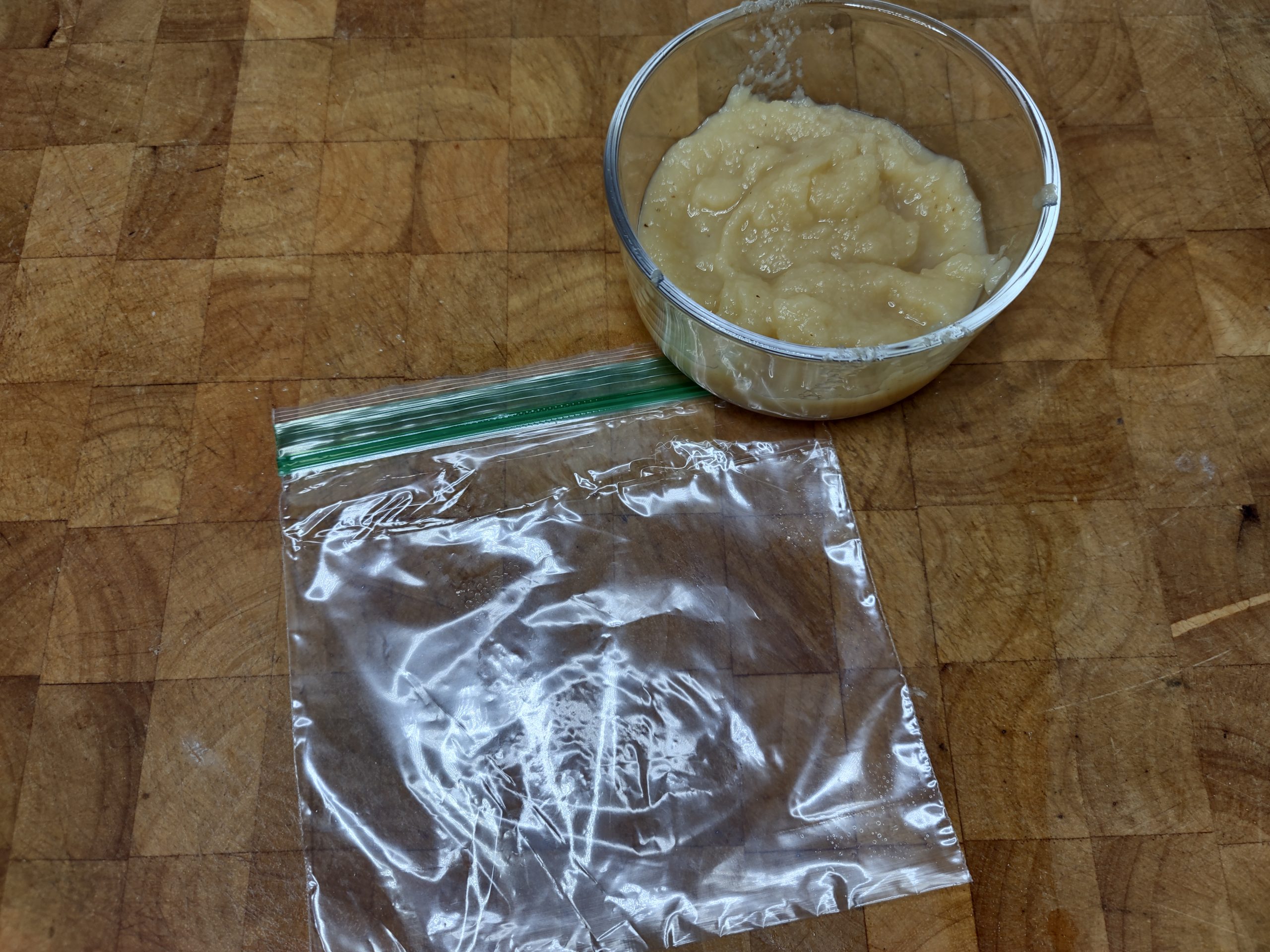 bowl of applesauce sitting next to an empty freezer bag on a wooden table