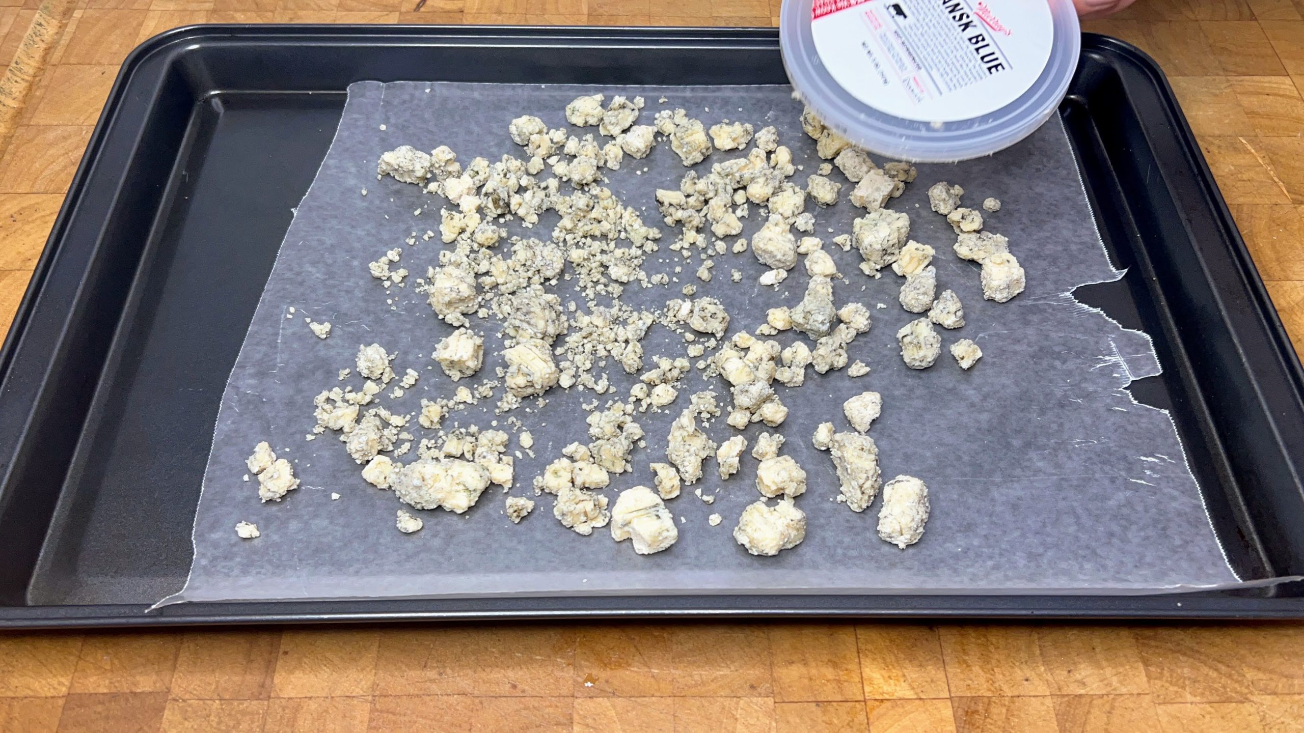 blue cheese crumbles spread on parchment paper on cookie sheet