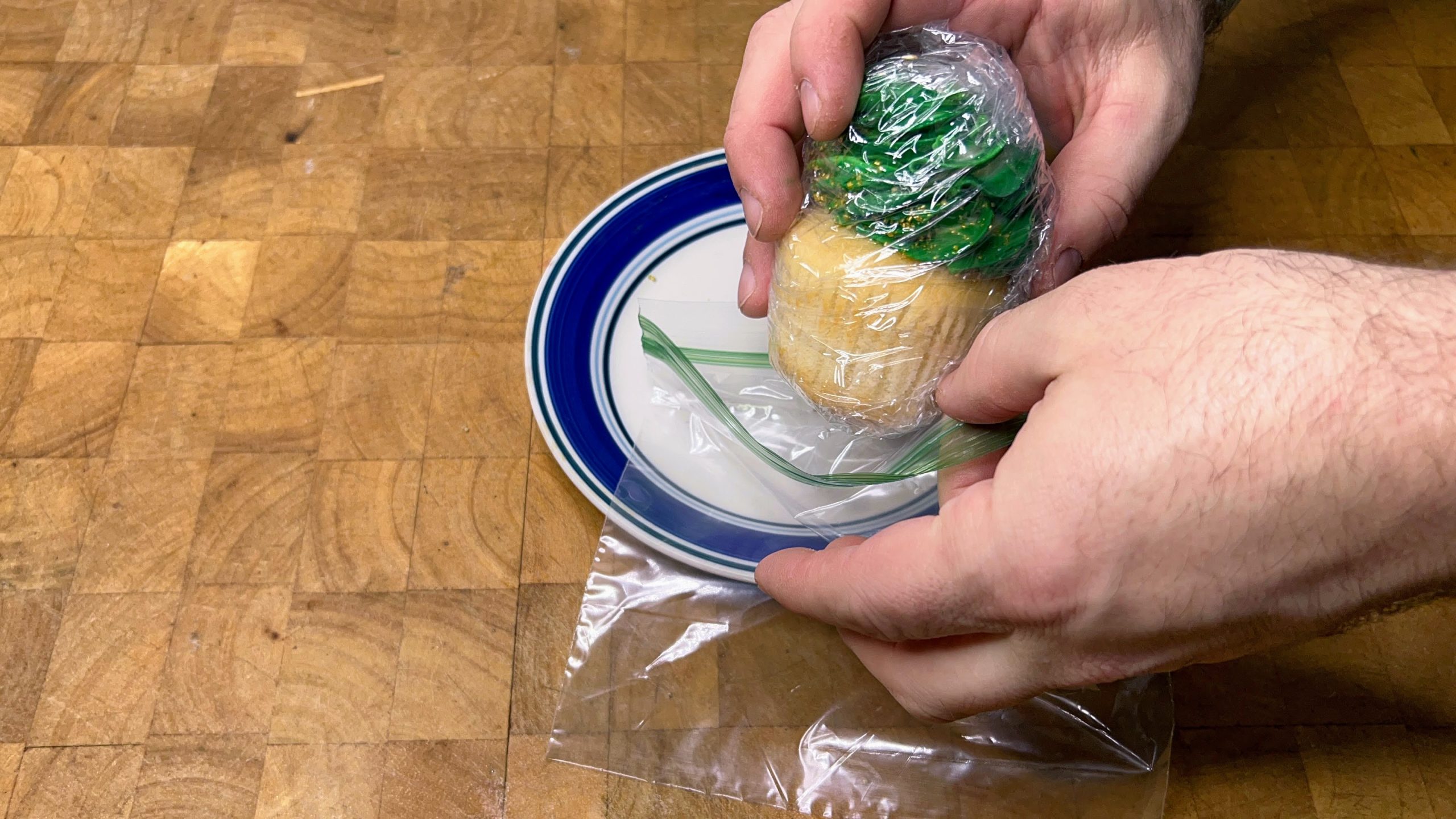 placing plastic wrapped cupcake with buttercream frosting into a freezer bag