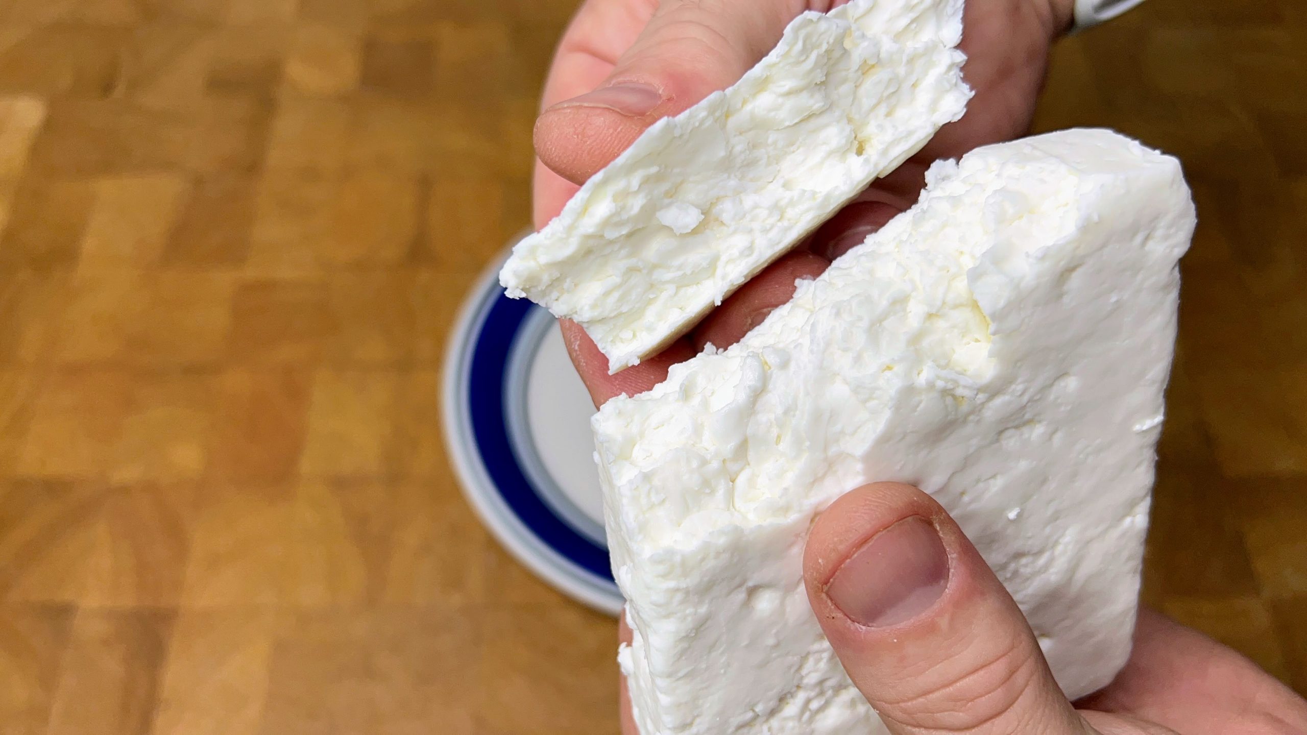holding a block of defrosted feta cheese with a piece broken off