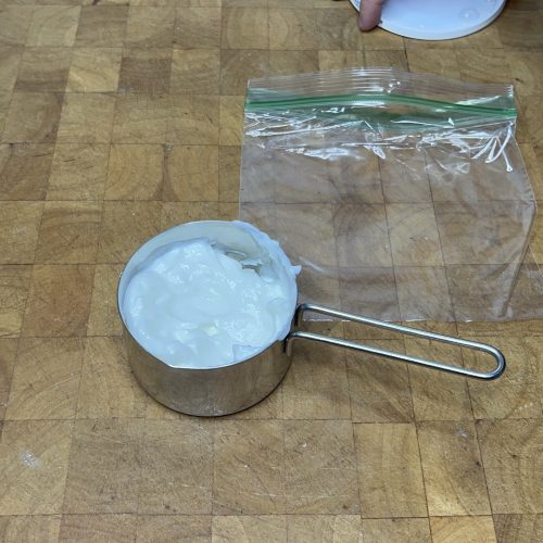 measuring cup full of greek yogurt next to an empty freezer bag