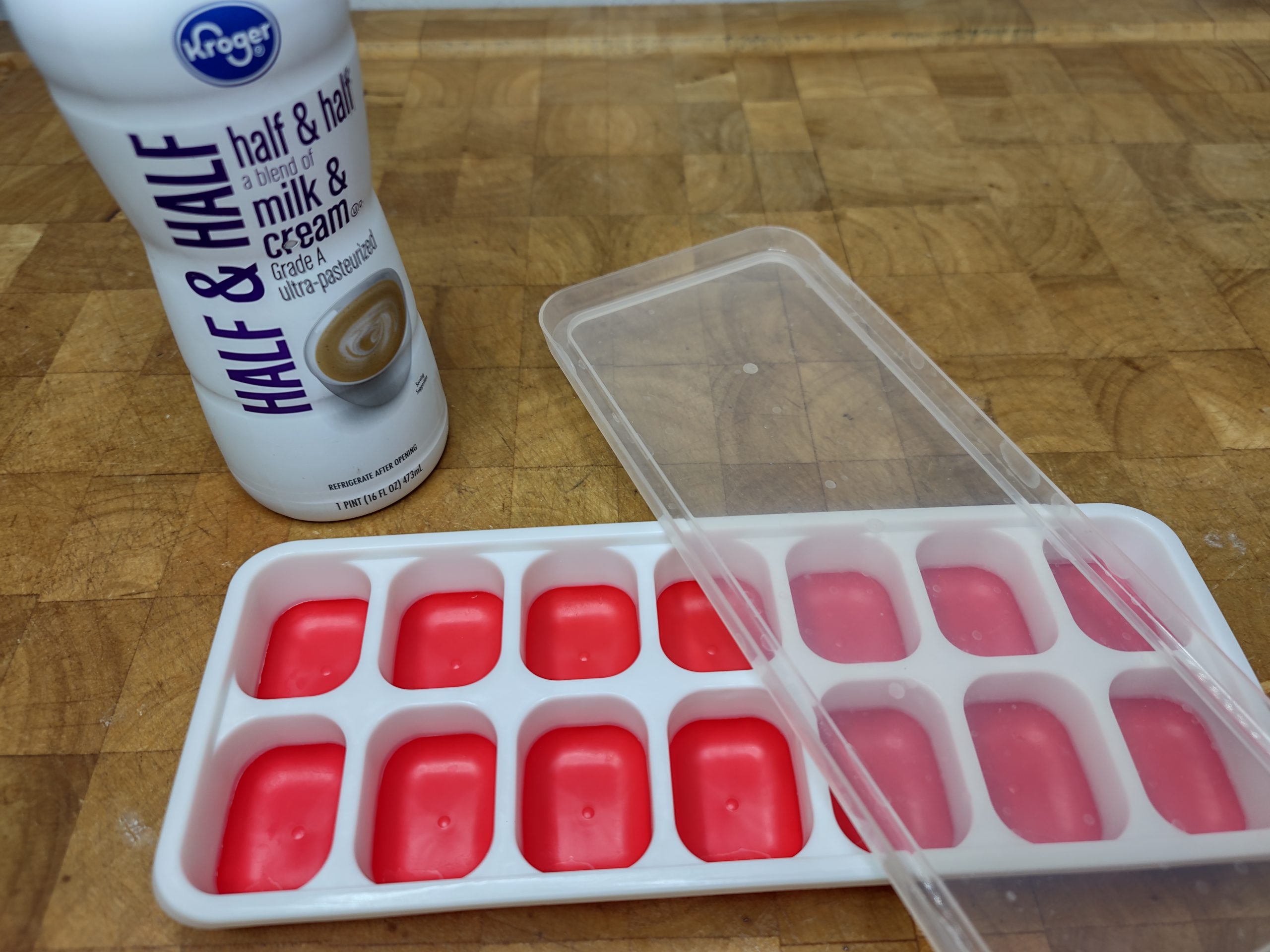 bottle of half and half next to an empty ice cube tray with a lid on a wooden table