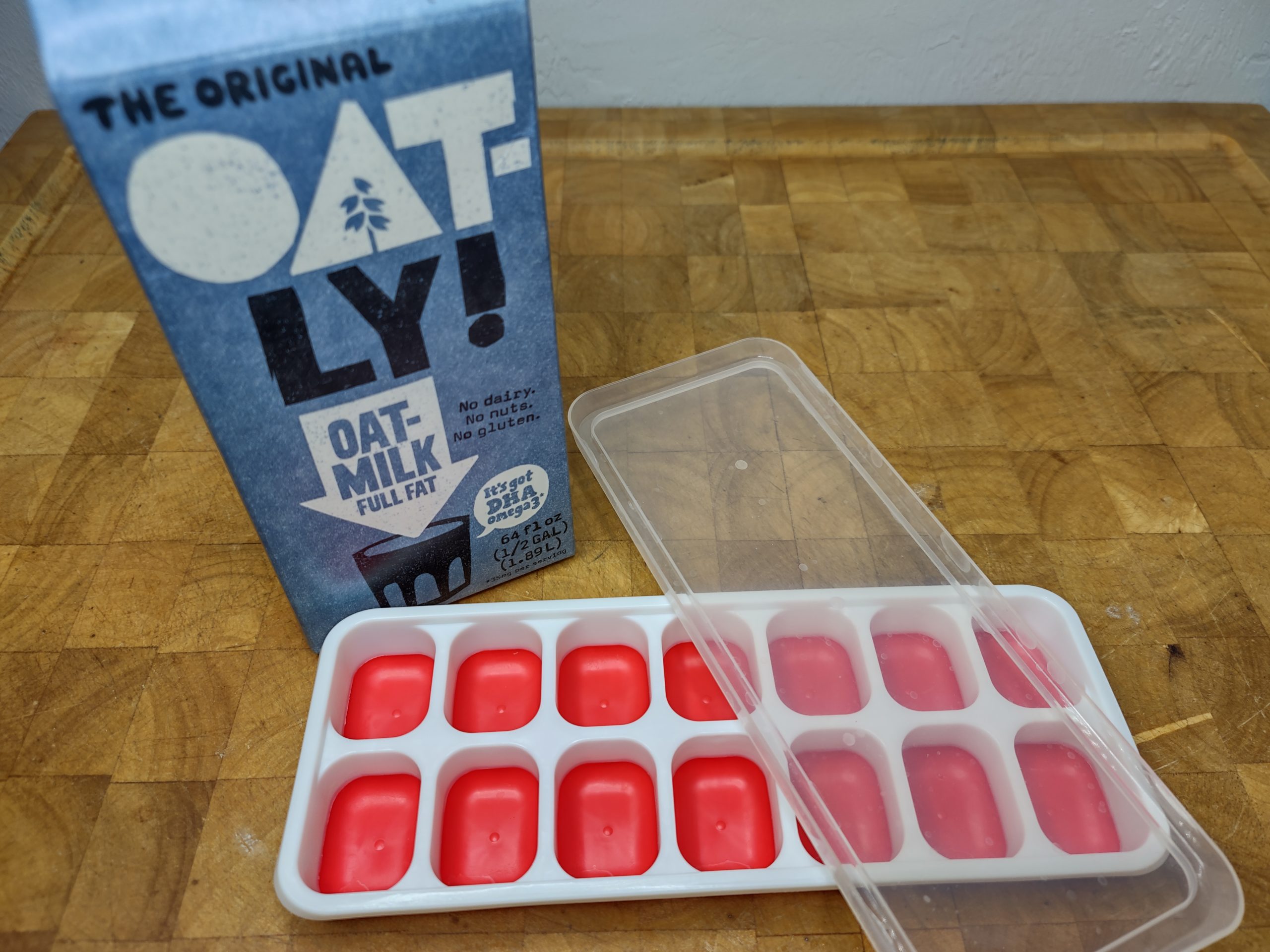 carton of oat milk sitting behind an empty ice cube tray with a lid on it