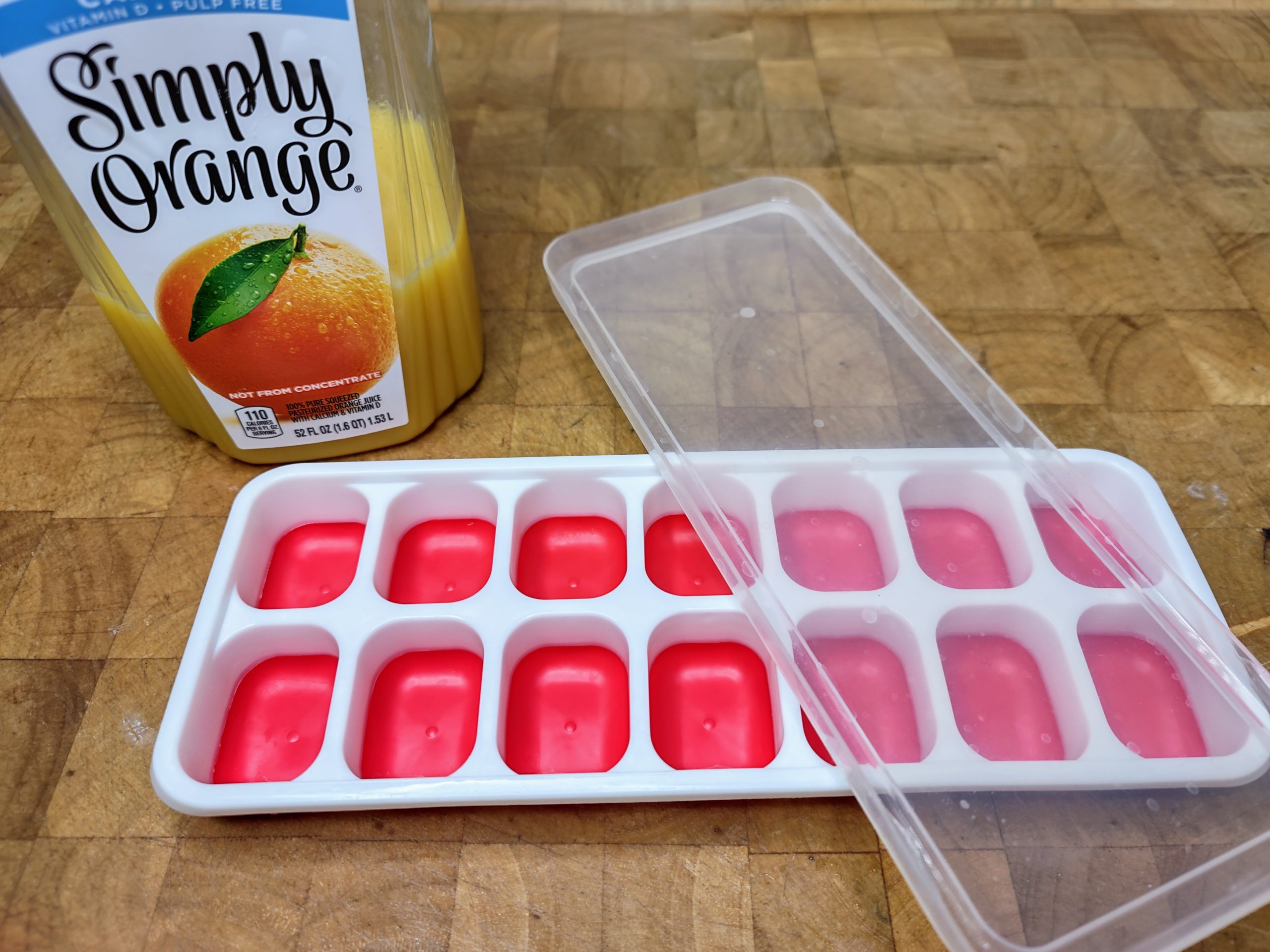bottle of orange juice sitting behind an empty ice cube tray with a lid on a wooden table
