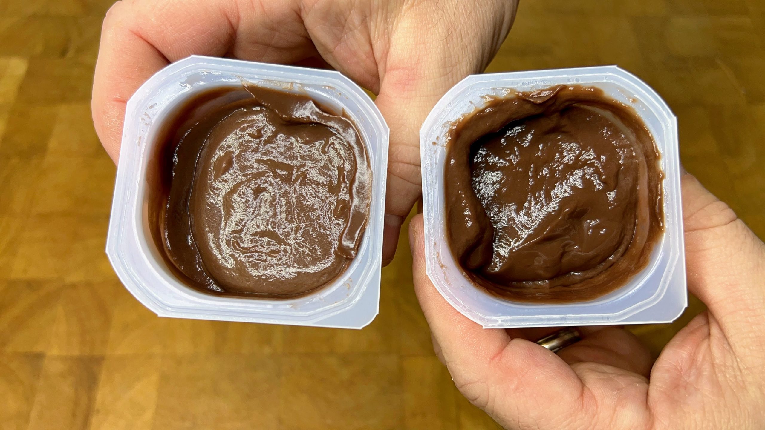 hands holding two containers of pudding: defrosted pudding on left, fresh pudding on right
