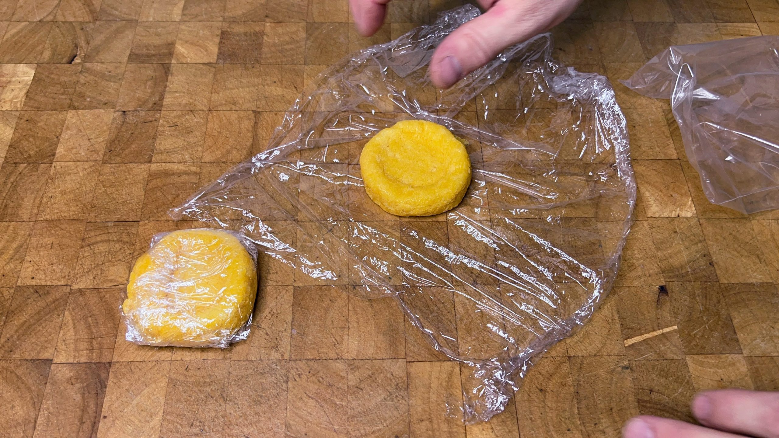 two sponge cakes sitting on plastic wrap on a wooden table