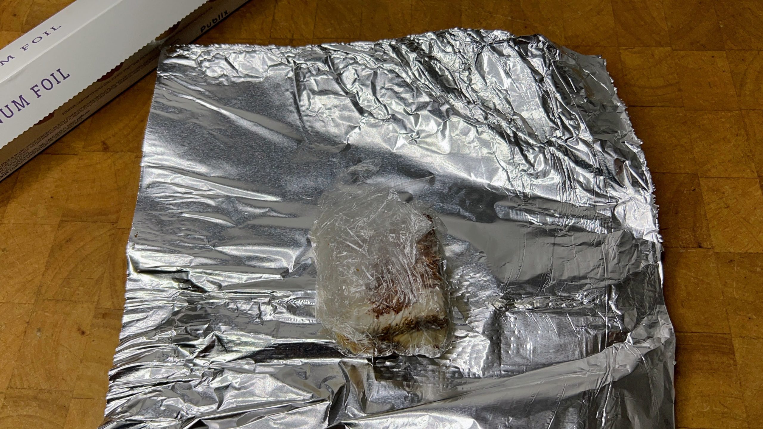 plastic wrapped tiramisu sitting in the center of a sheet of aluminum foil