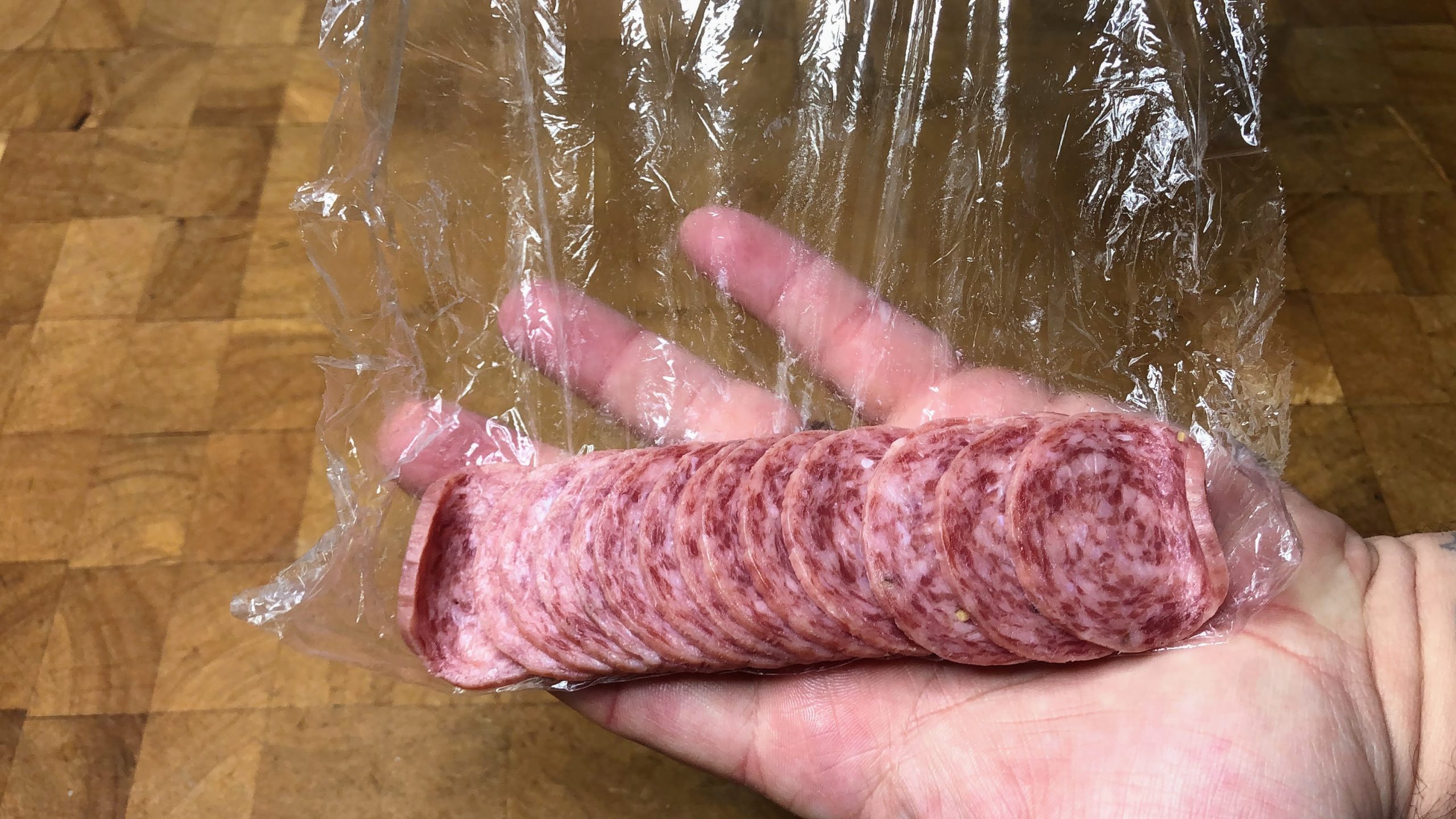 stack of defrosted salami with plastic wrap behind it