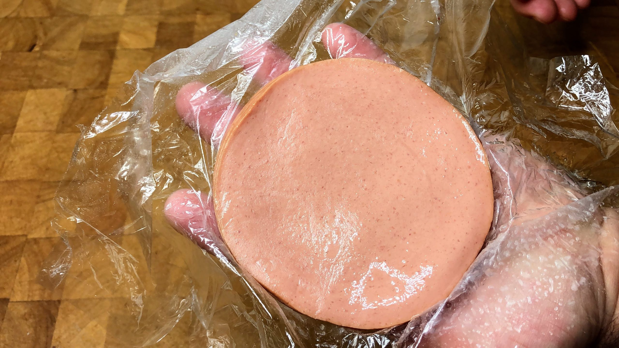 defrosted stack of bologna being held on a sheet of plastic wrap