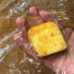 slice of cornbread being held on a sheet of plastic wrap