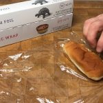 hot dog bun sitting on a sheet of plastic wrap on a wooden table