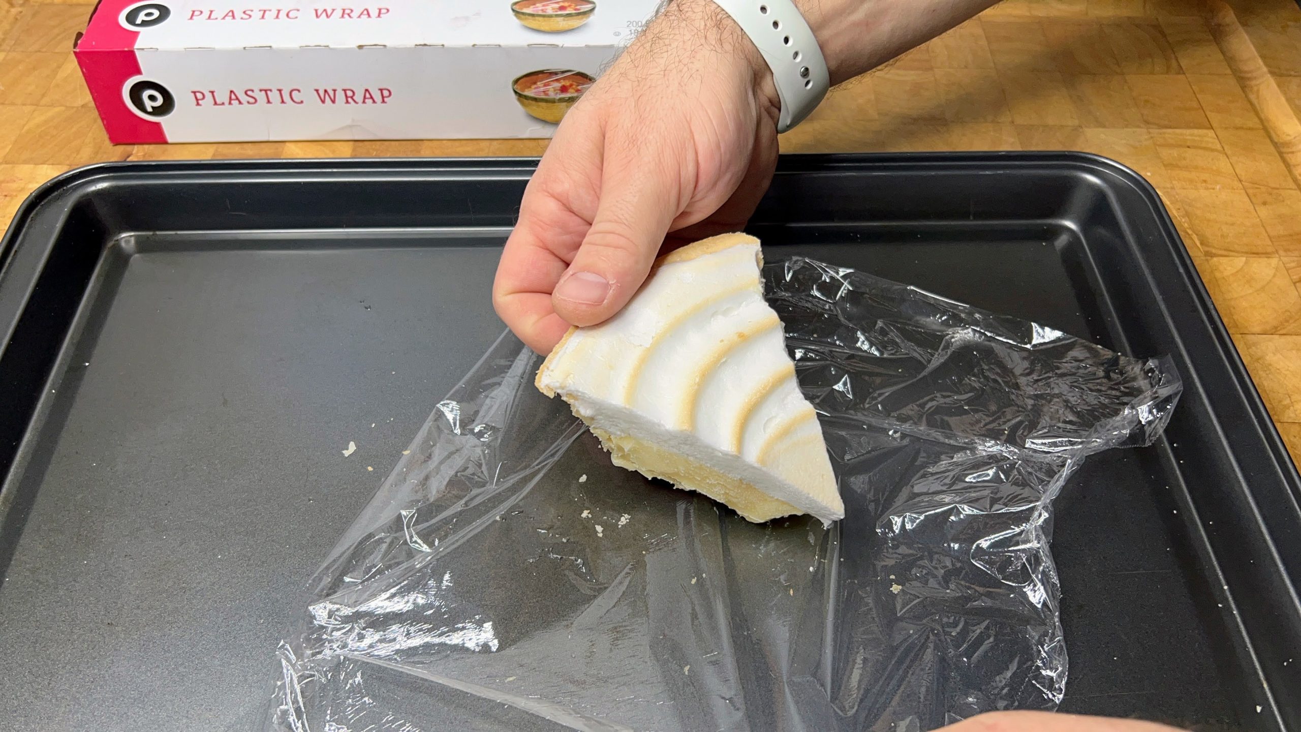 slice of lemon meringue pie sitting on a sheet of plastic wrap on a cookie sheet