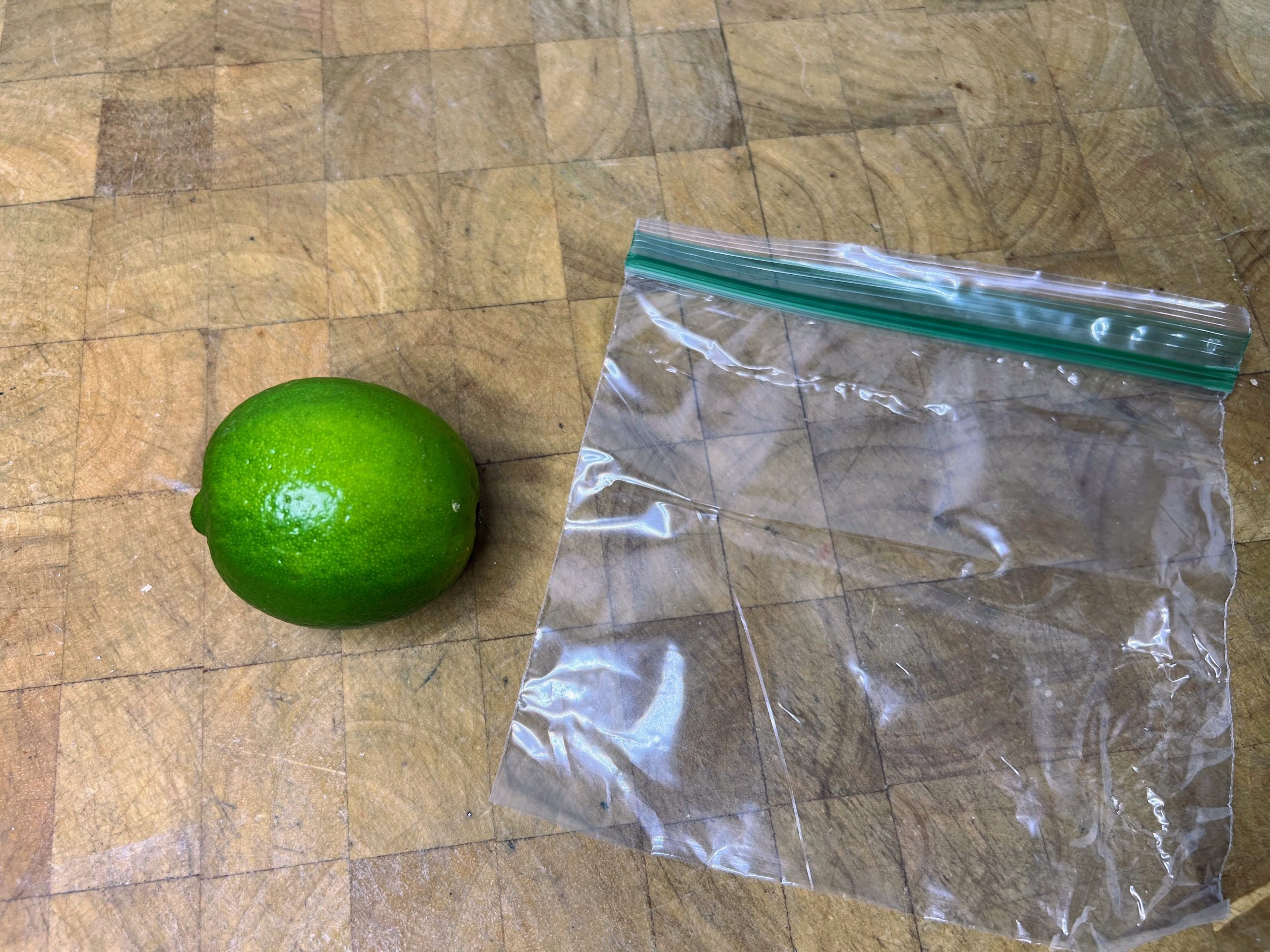 whole lime next to an empty freezer bag on a wooden table