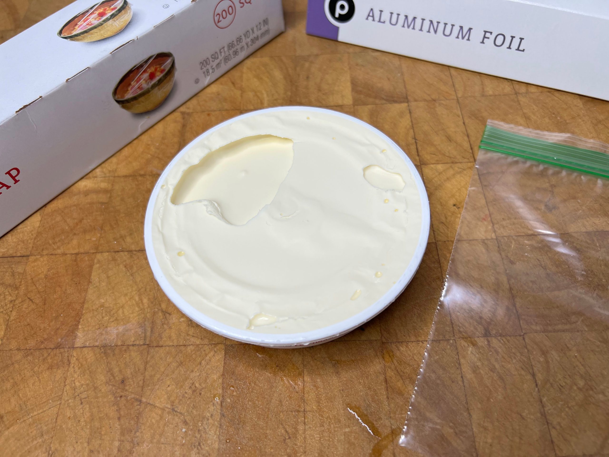 container of mascarpone cheese next to an empty freezer bag, plastic wrap and aluminum foil