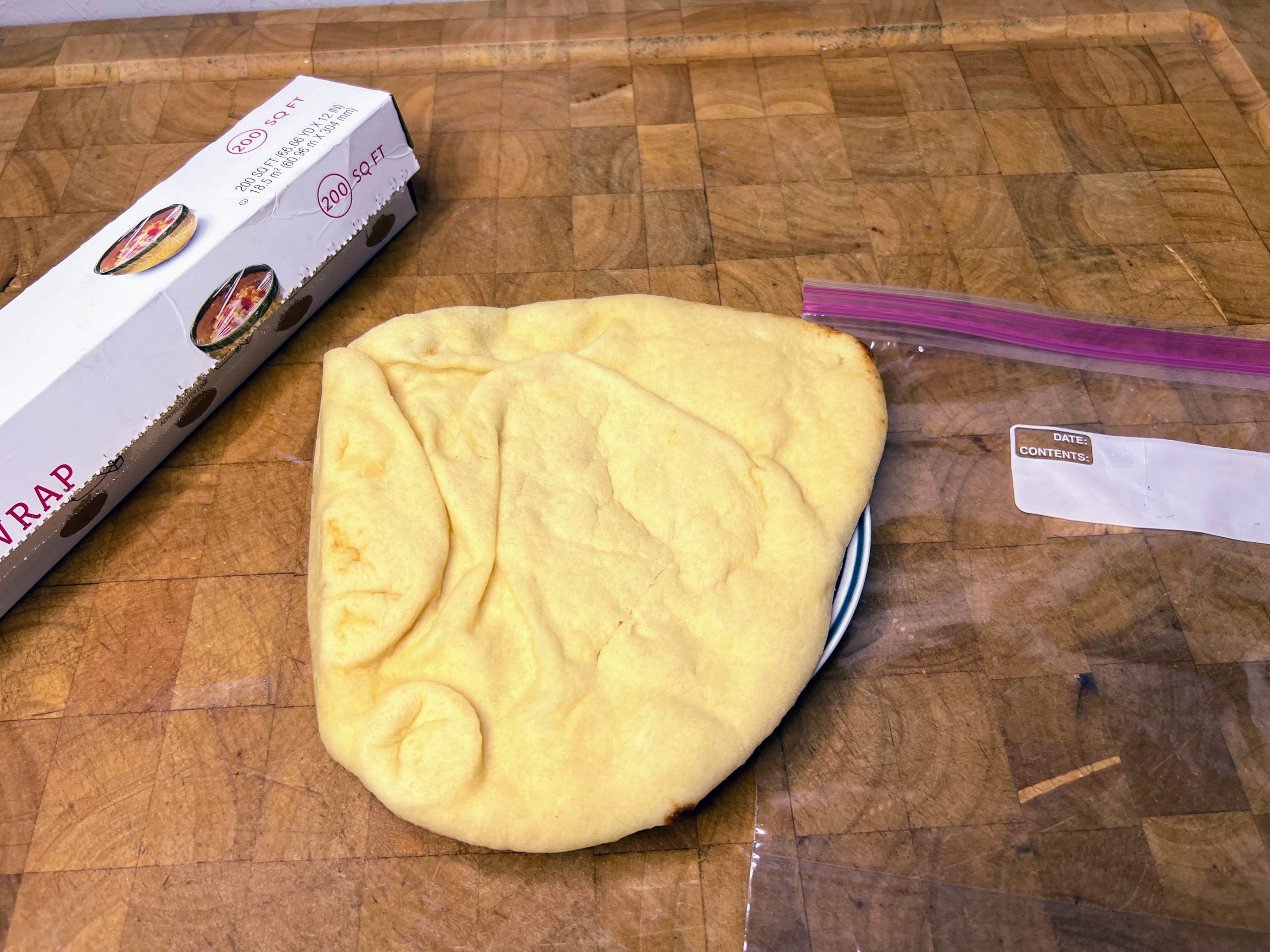 naan bread on a plate next to an empty freezer bag and plastic wrap