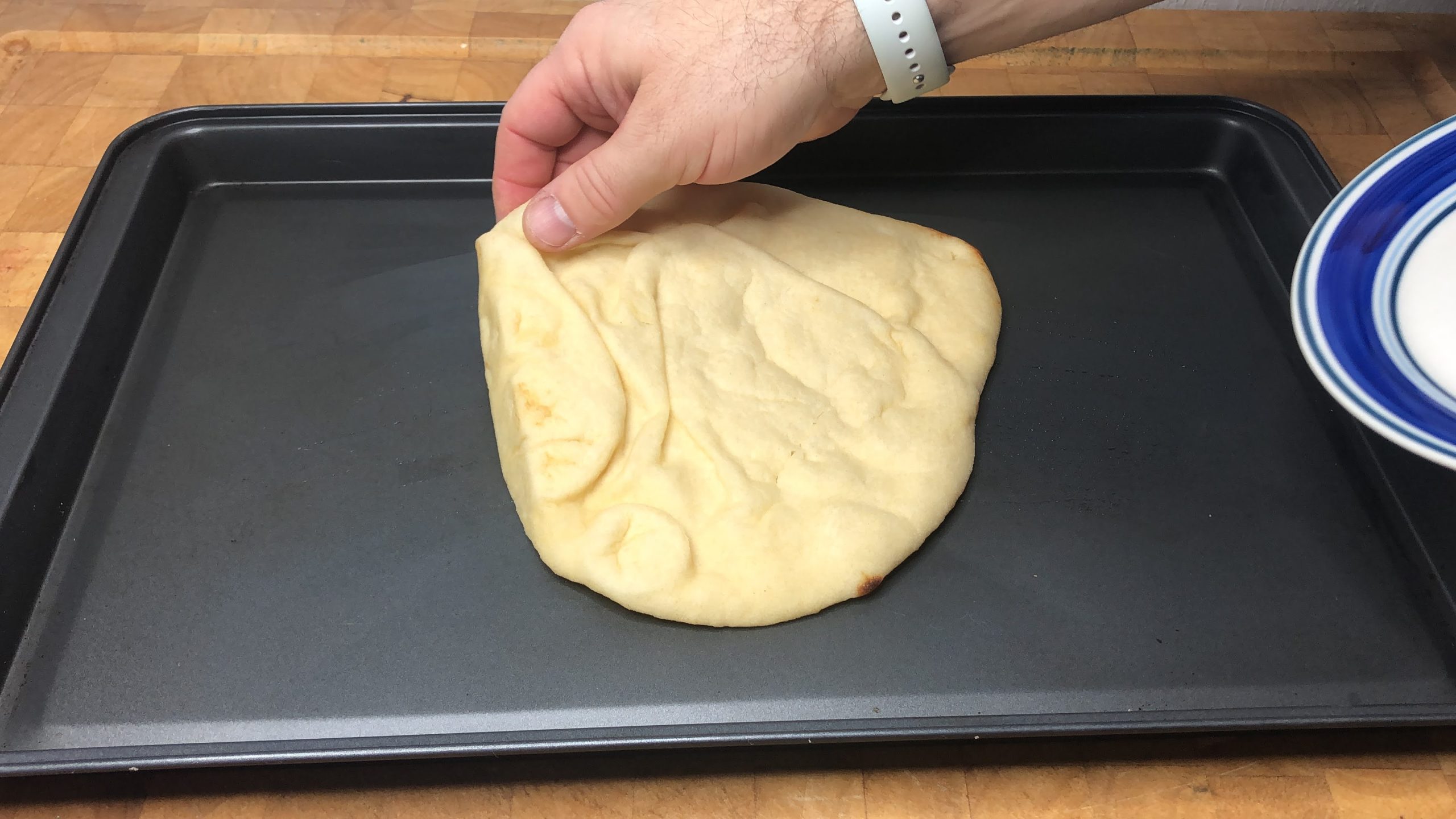 laying a slice of naan bread on a cookie sheet