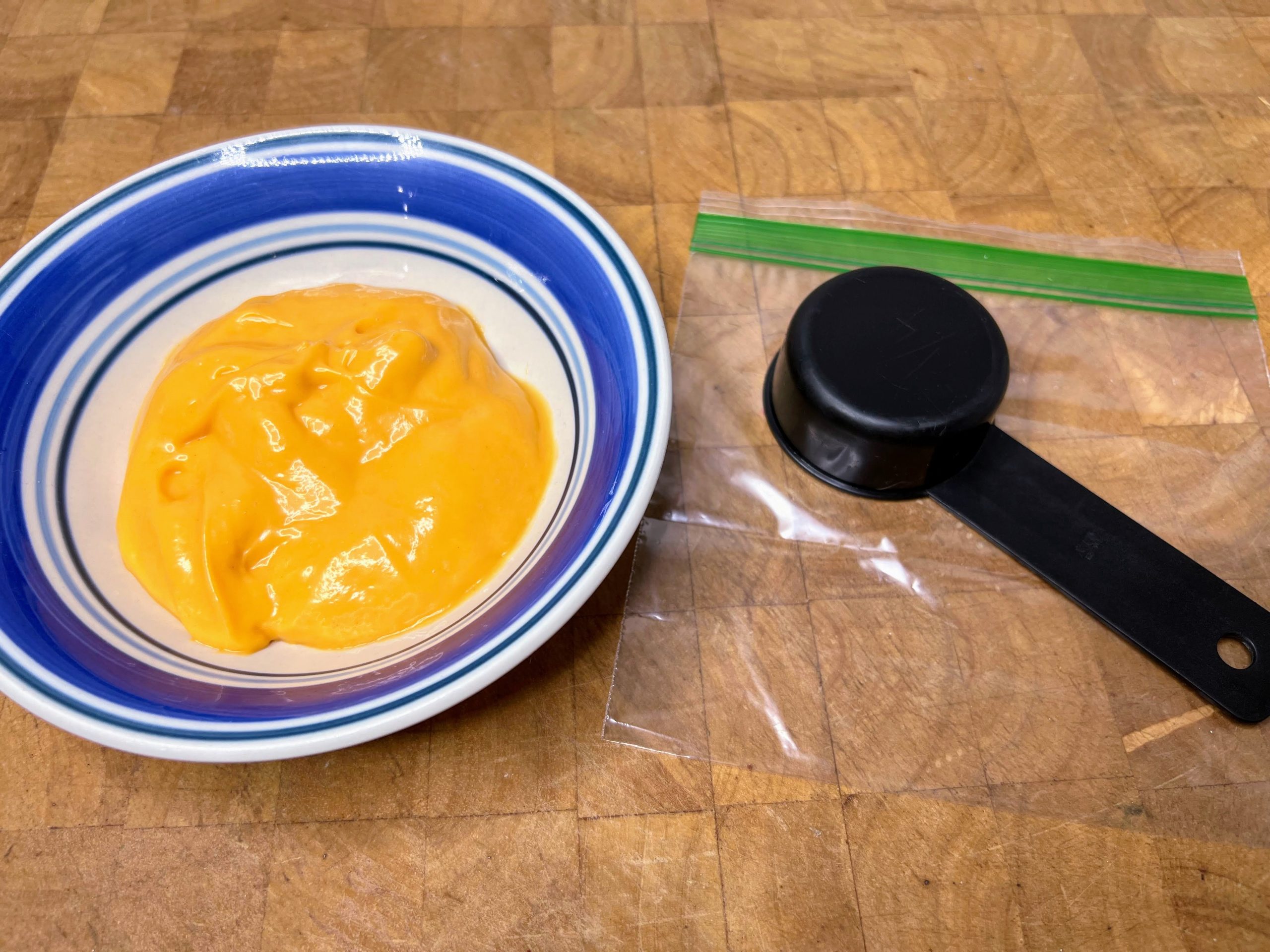 bowl of nacho cheese next to an empty freezer bag and a measuring cup