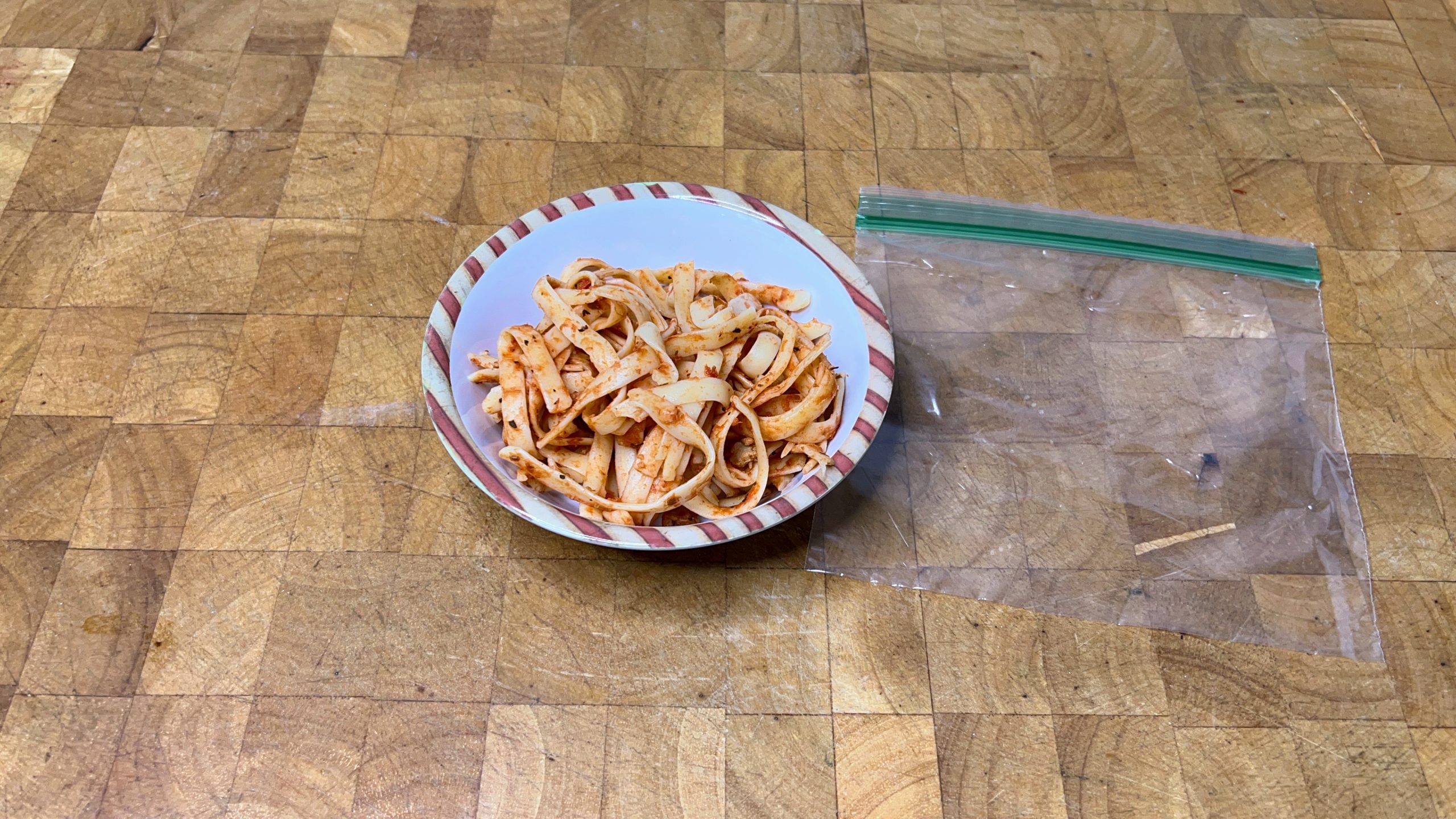 bowl of spaghetti next to an empty freezer bag on a wooden table